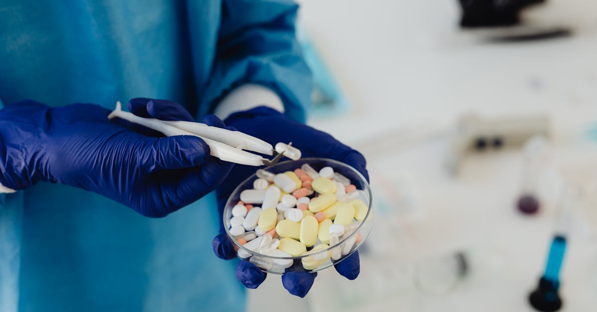 Scientist in gloves using tweezers to handle assorted pills in a petri dish. Scientist in gloves using tweezers to handle assorted pills in a petri dish.