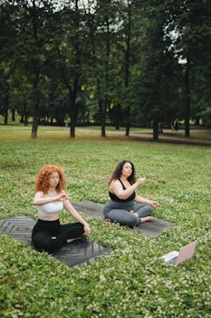 Two women meditating on yoga mats in a serene park, engaging in outdoor recreation.