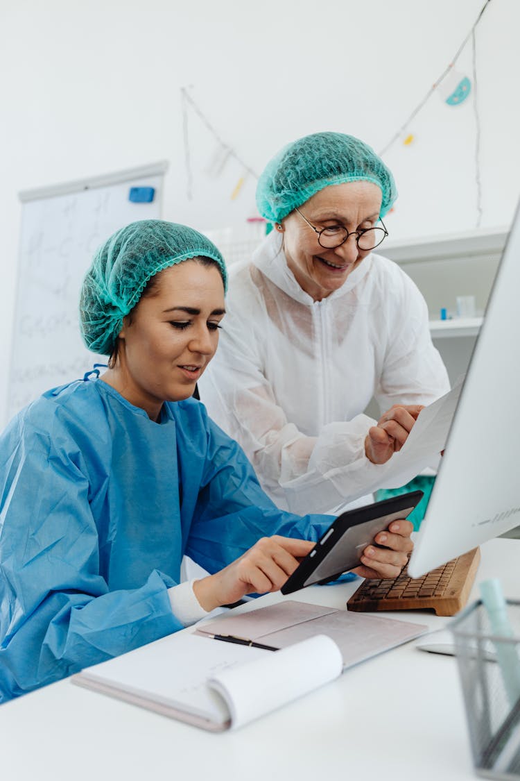 A Pair Of Women Wearing Bouffant Caps And A White And Blue Surgical Gowns