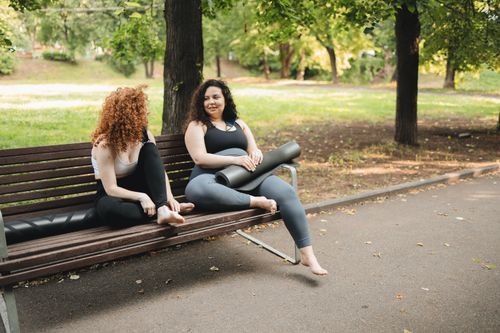 Free Two women sitting on a park bench chatting after a yoga session. Stock Photo