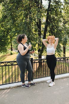Two women standing outdoors by a railing, enjoying post-exercise relaxation.