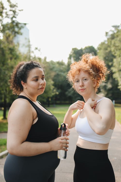 Free Two women in activewear stand outdoors holding a water bottle, enjoying a sunny day in the park. Stock Photo