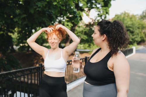 Free Two women in activewear enjoying a summer workout in the park, staying hydrated with water. Stock Photo