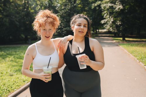 Free Two women in activewear enjoying drinks and friendship in a sunny park. Stock Photo