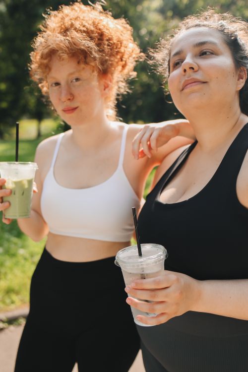 Free Two women relaxing outdoors with drinks, embodying friendship and togetherness in a sunny park setting. Stock Photo