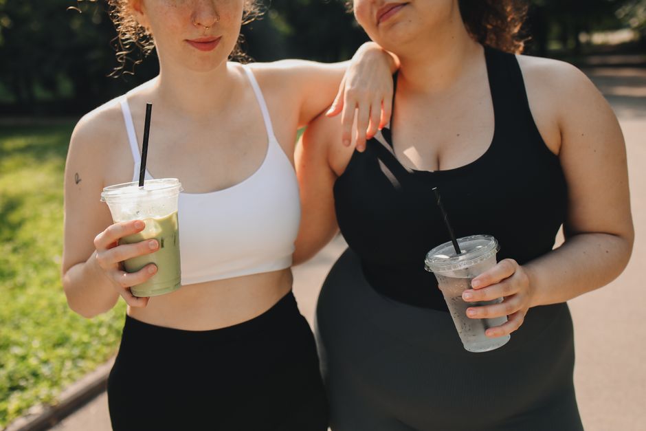 Two women in activewear enjoying drinks in a sunny outdoor setting.