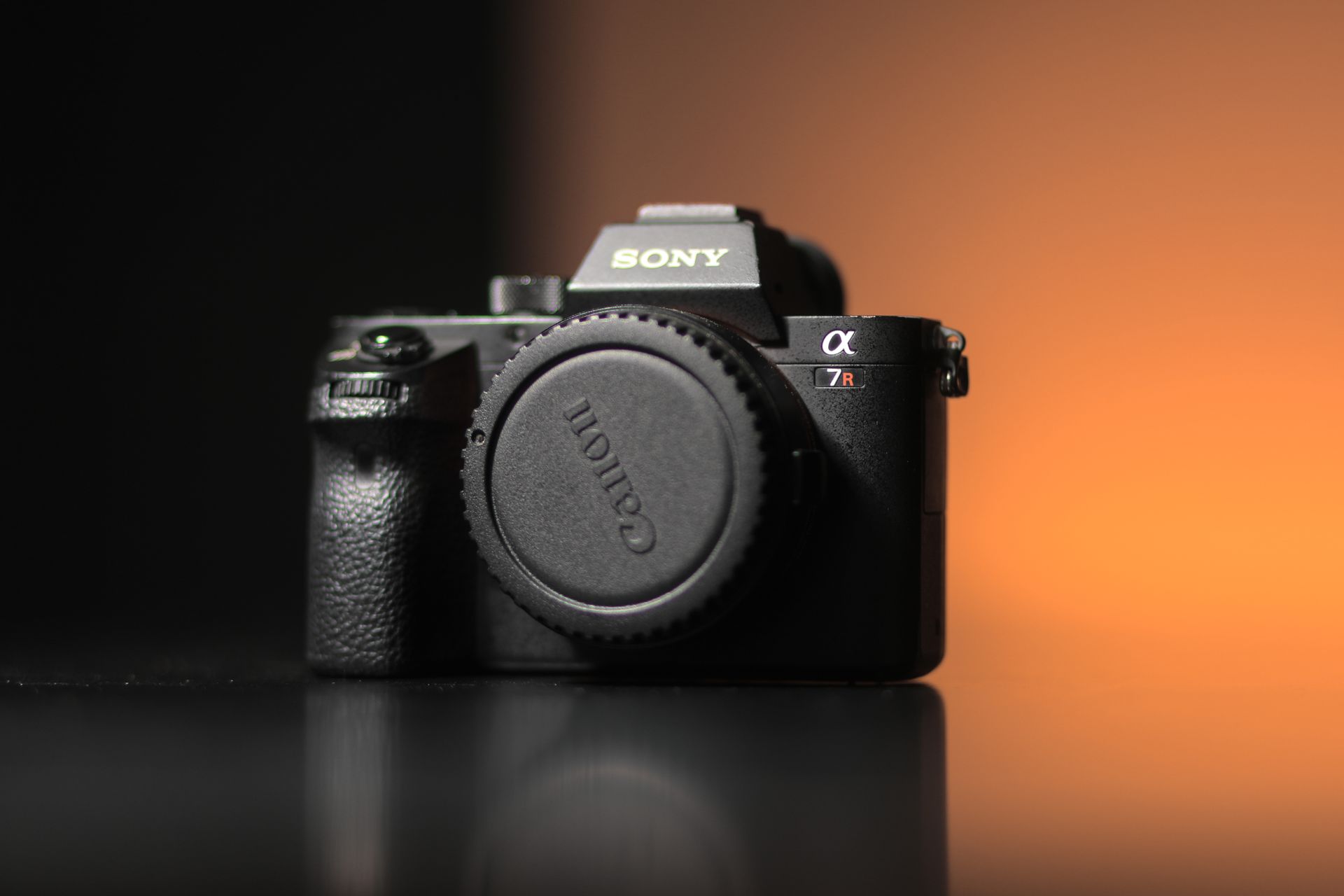 Close-up of a Sony camera with a Canon lens cap on a sleek surface.