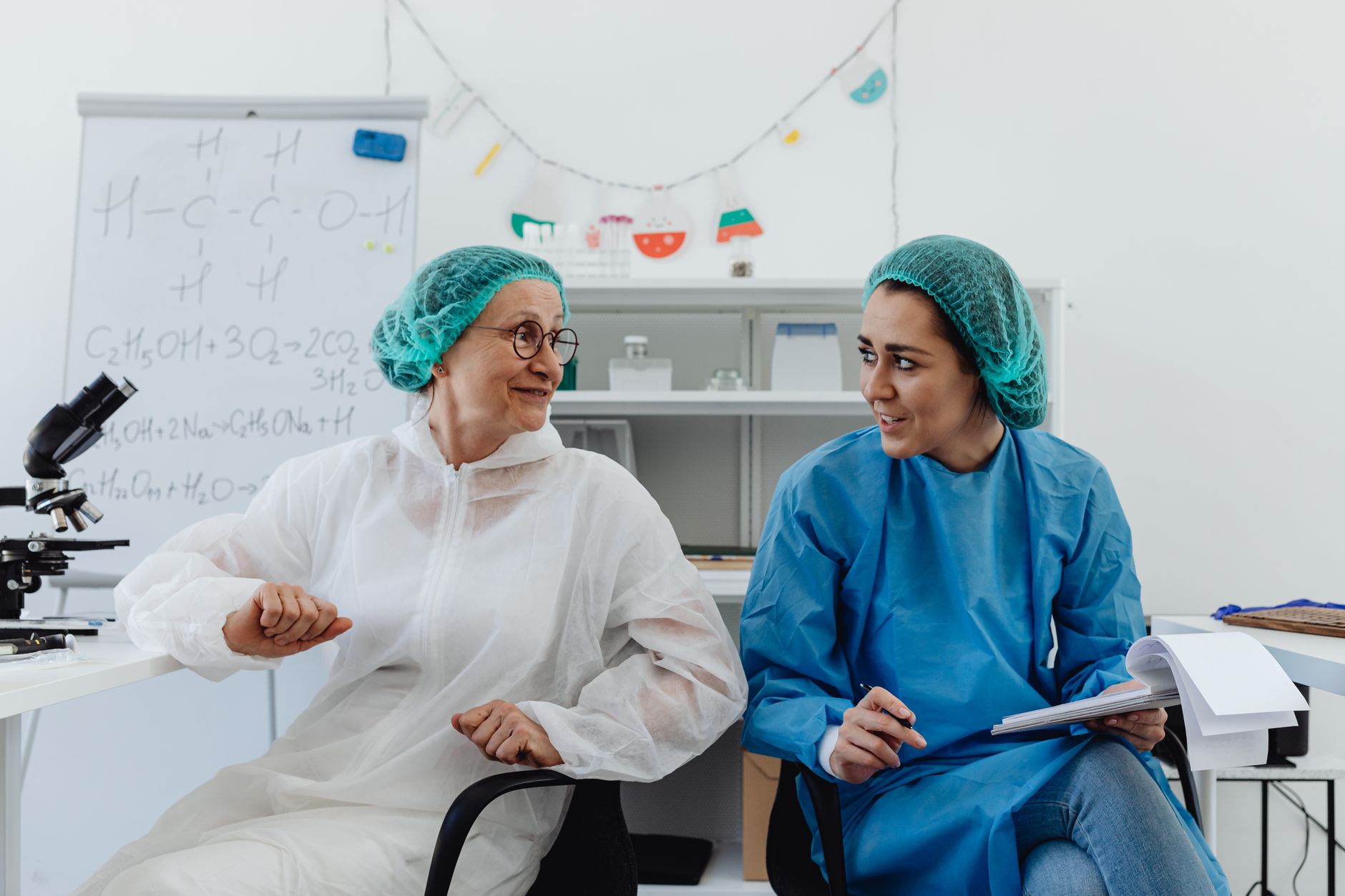 Two female scientists in conversation, wearing protective gear in a modern laboratory setting.