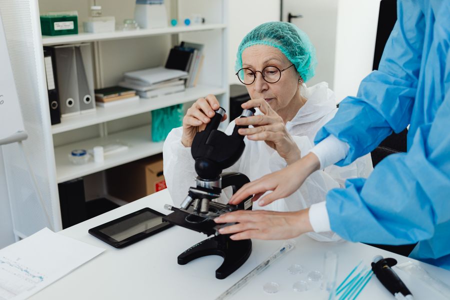 Senior researcher working with a microscope in a laboratory setting, assisted by a colleague.