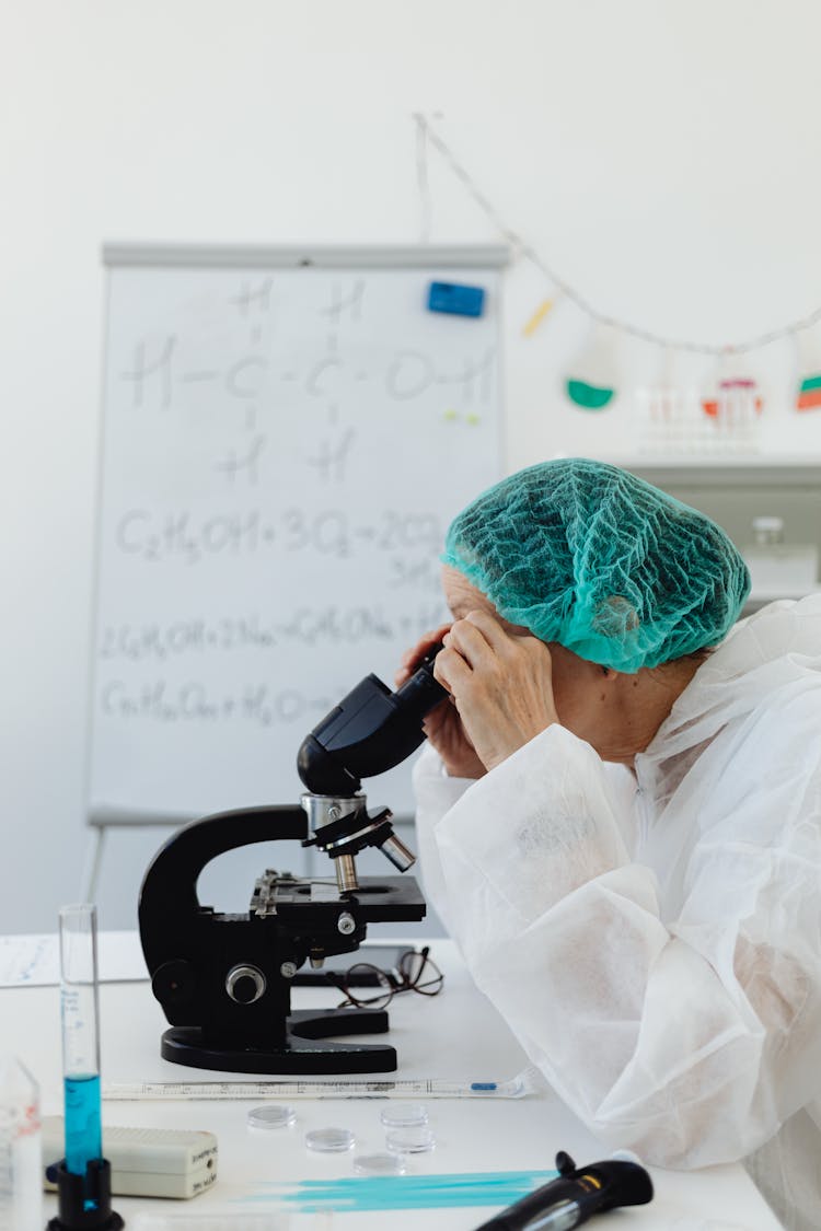 Person In White Scrub Suit Looking At The Microscope 