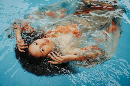 Free A serene portrait of an Asian woman floating in a pool, wearing a colorful dress. Stock Photo