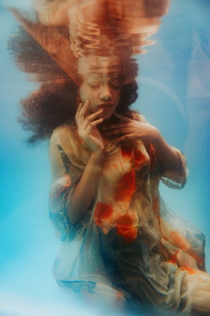 Artistic underwater photo of woman in floral dress, eyes closed, serene expression.