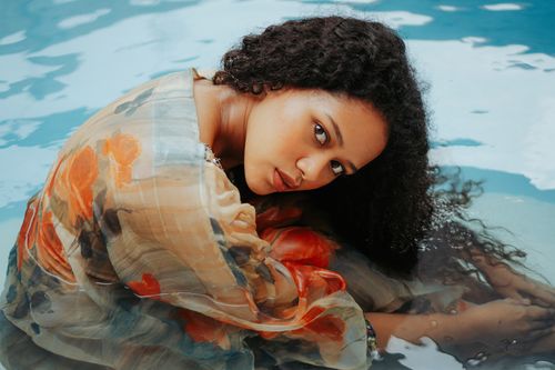 Free Asian woman with curly hair in floral dress submerged in swimming pool. Stock Photo