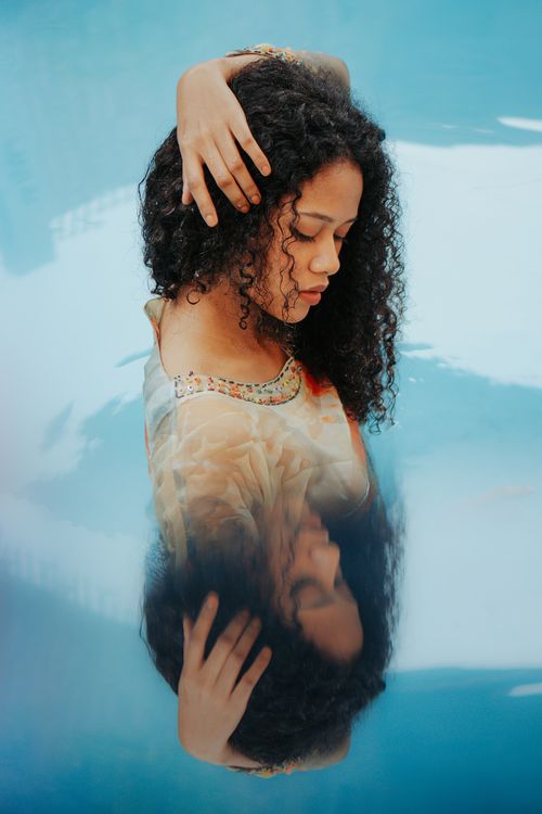 Free Dreamy portrait of a woman with curly hair reflected in a swimming pool. Stock Photo