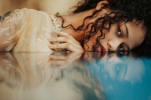 Free Artistic photo capturing a woman's reflection in water, emphasizing curly hair and creative light play. Stock Photo