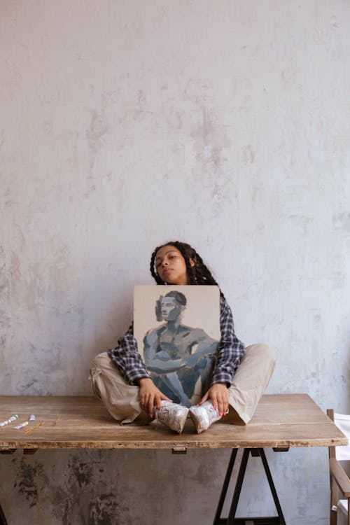 Woman Sitting on a Table while Embracing an Artwork
