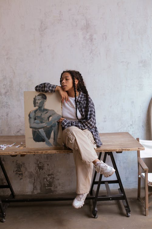 A Young Woman Sitting on a Wooden Table while Holding a Painting 