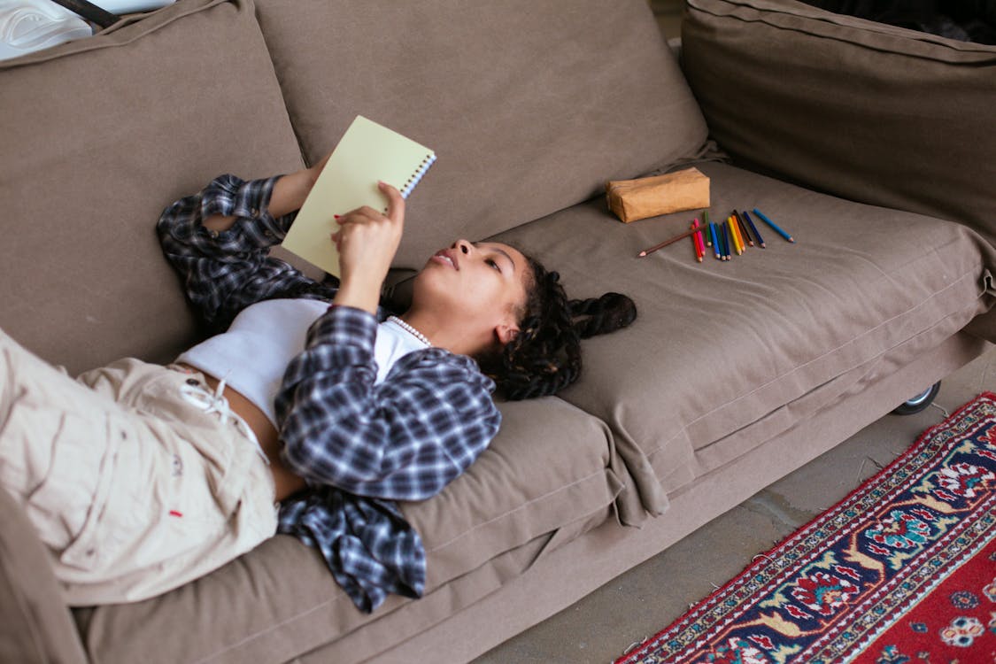 A Woman in Plaid Long Sleeves Reading a Book while Lying on the Sofa