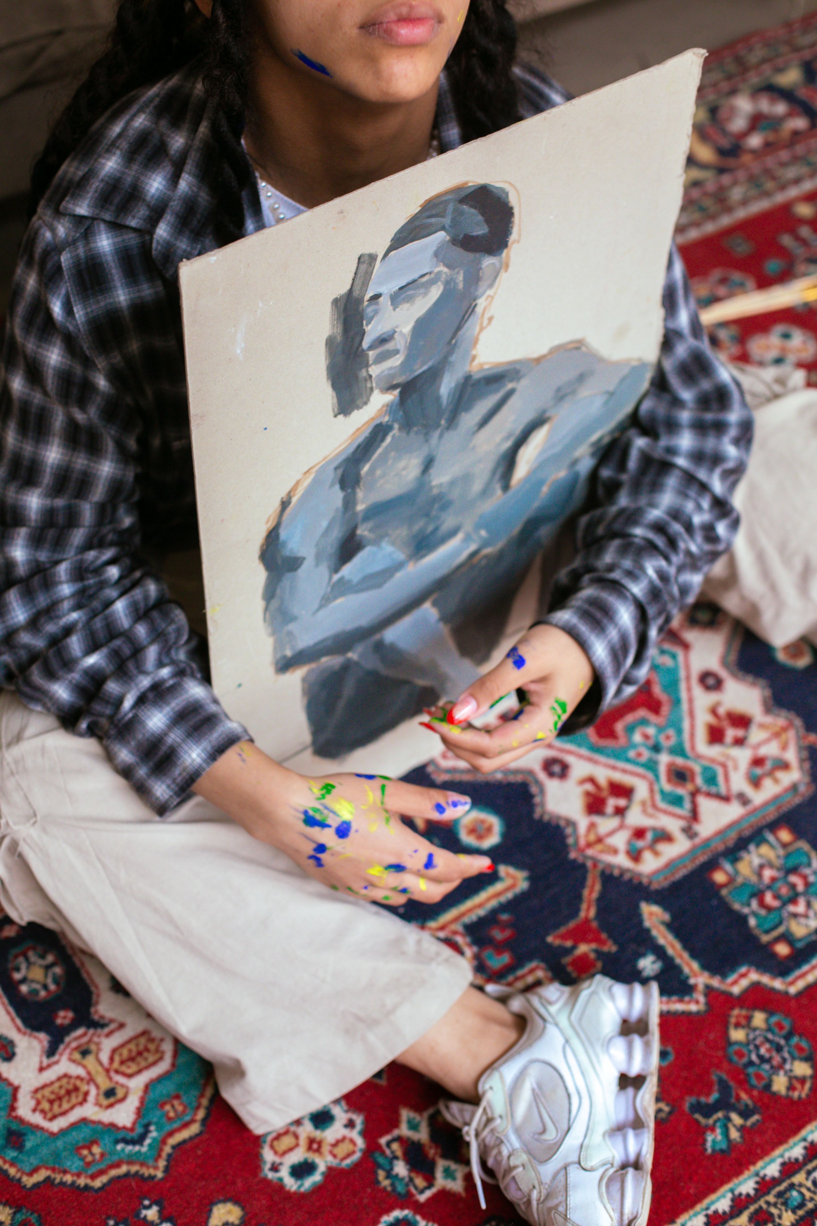 Young artist holding a painted canvas with colorful paint on hands, wearing plaid shirt.