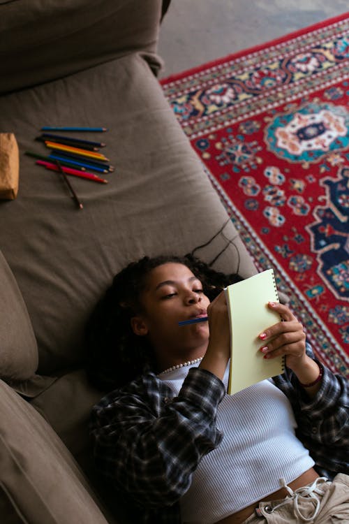 High-Angle Shot of a Woman Lying Down While Writing on a Notebook