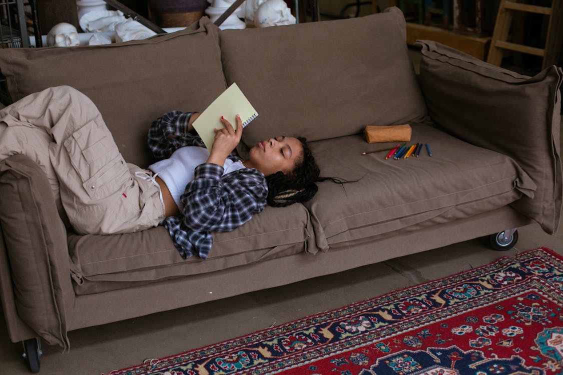 Teenage Girl Lying on Sofa While Holding a Notebook