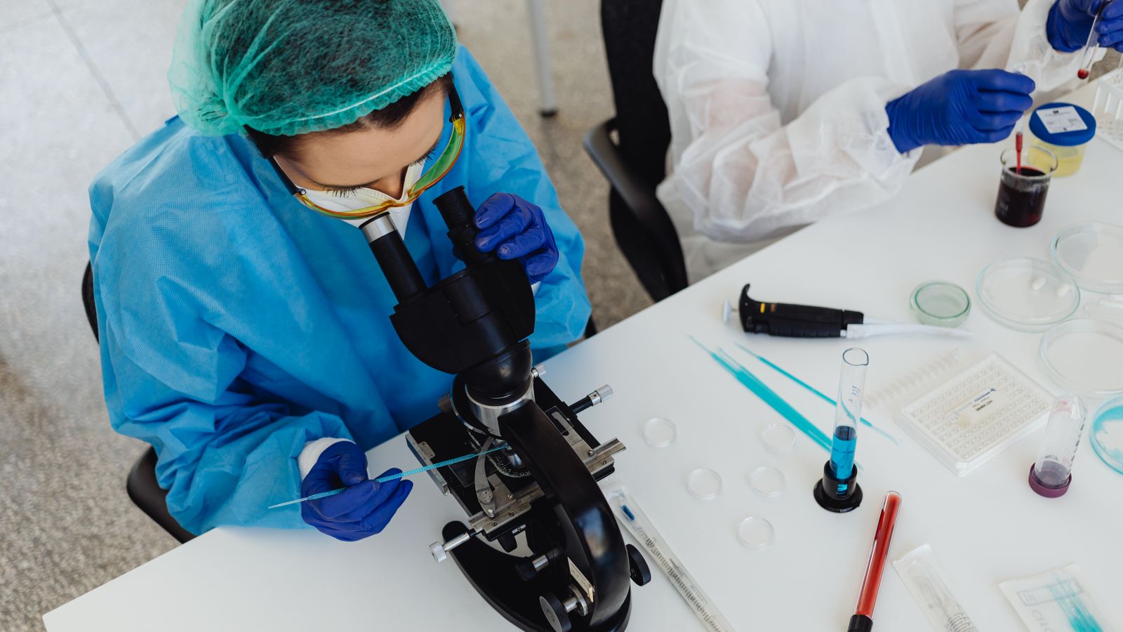 Researchers in PPE examining samples with a microscope in a laboratory setting.