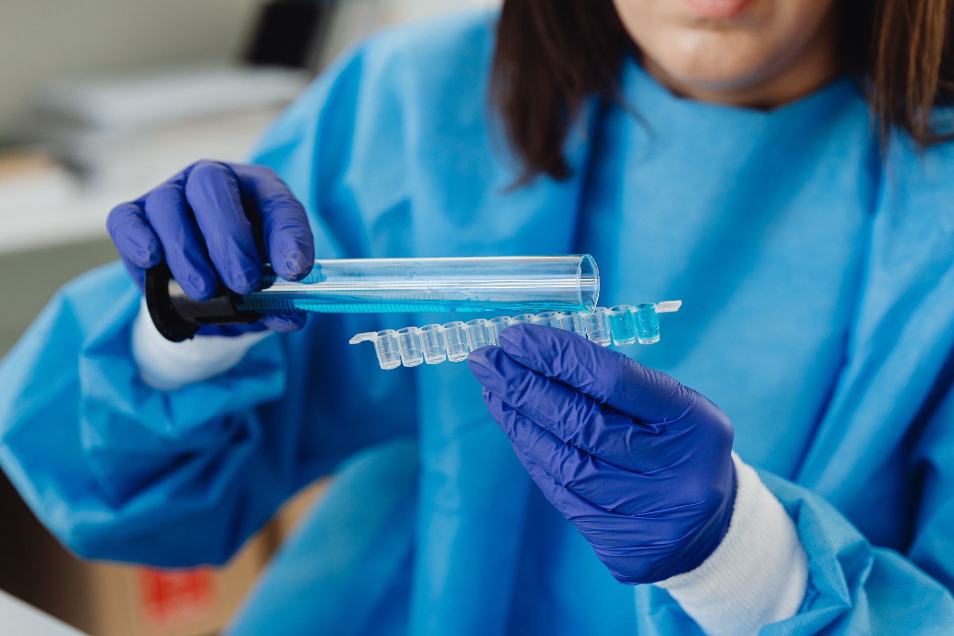 Scientist in blue protective gear conducting laboratory analysis with test tubes and vials.