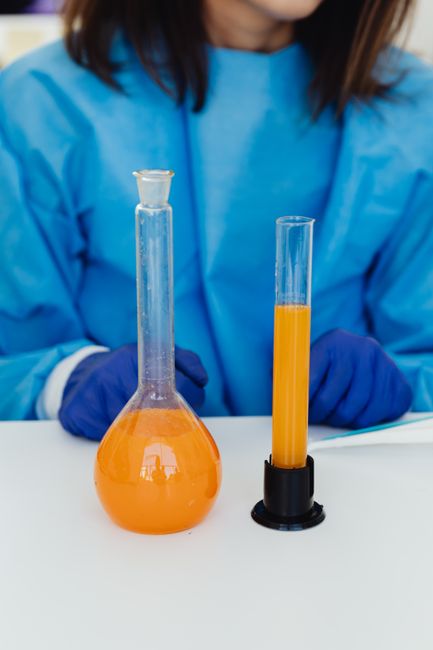 Close-up of a scientist working with orange liquid in glass lab equipment.
