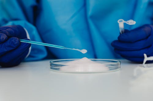 Hands of a Person in Blue Gloves Holding Glass Tools