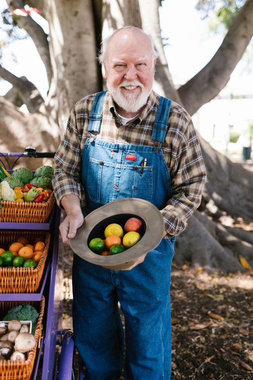 Free Senior farmer holding a hat full of fresh citrus fruits at an outdoor market. Stock Photo