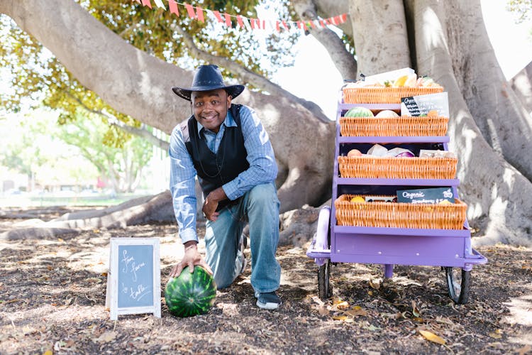 A Man Wearing A Hat Holding A Watermelon