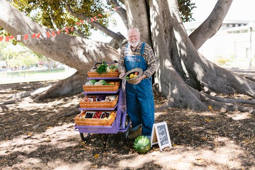 Free A Man Holding a Hat With Fruits Standing Near a Fruit Stand Stock Photo