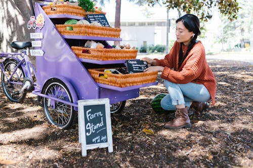 A Woman in Knitted Sweater and Denim Jeans Sitting Near the Cart with Woven Baskets