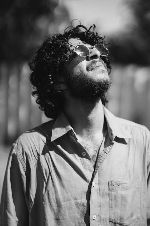 A Grayscale Photo of a Bearded Man Looking Up while Wearing Sunglasses