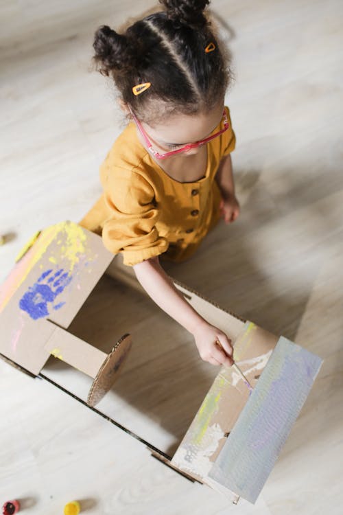 A Young Girl in Yellow Dress Painting a Carton Box