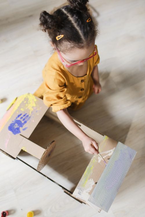 Free Young girl painting a cardboard box, engaged in a creative craft project indoors. Stock Photo