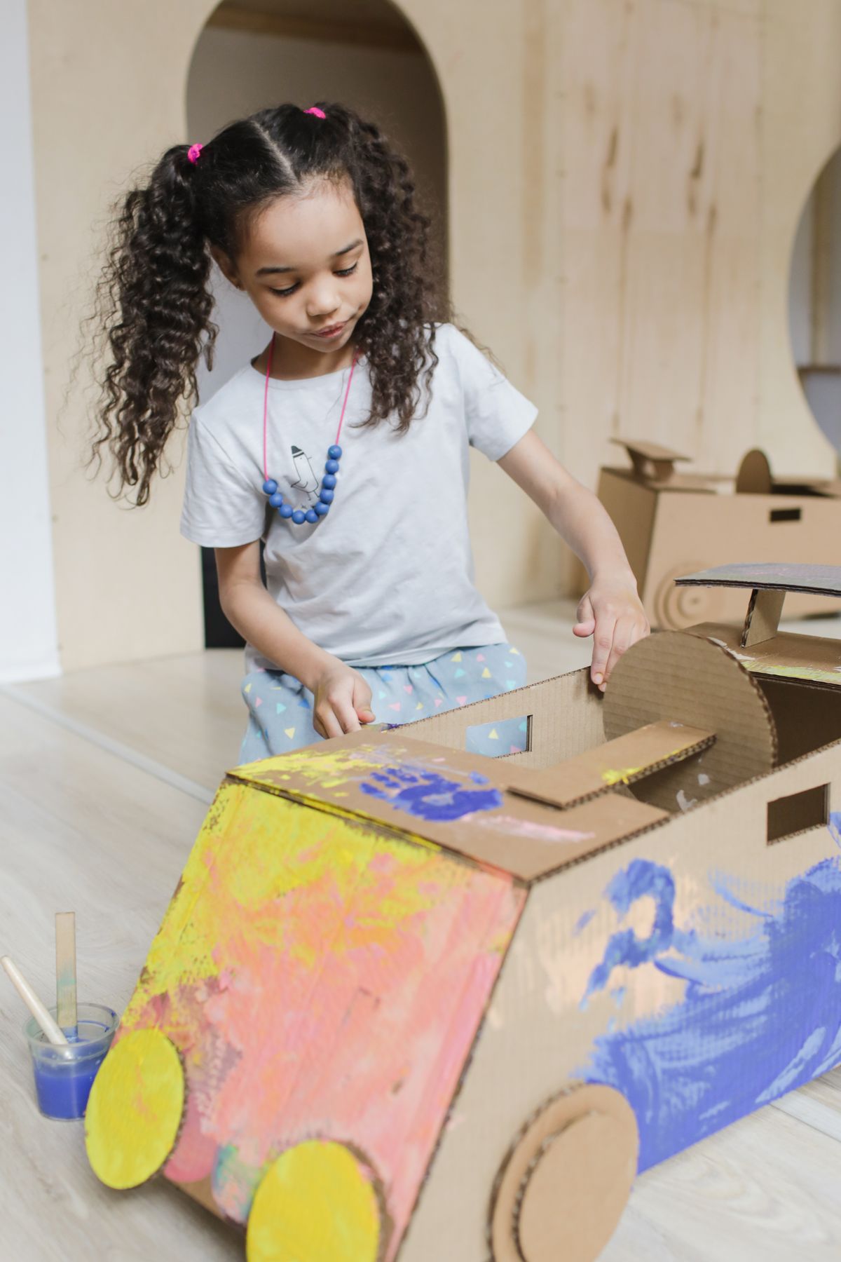 A young girl painting a large cardboard box to build a toy stable