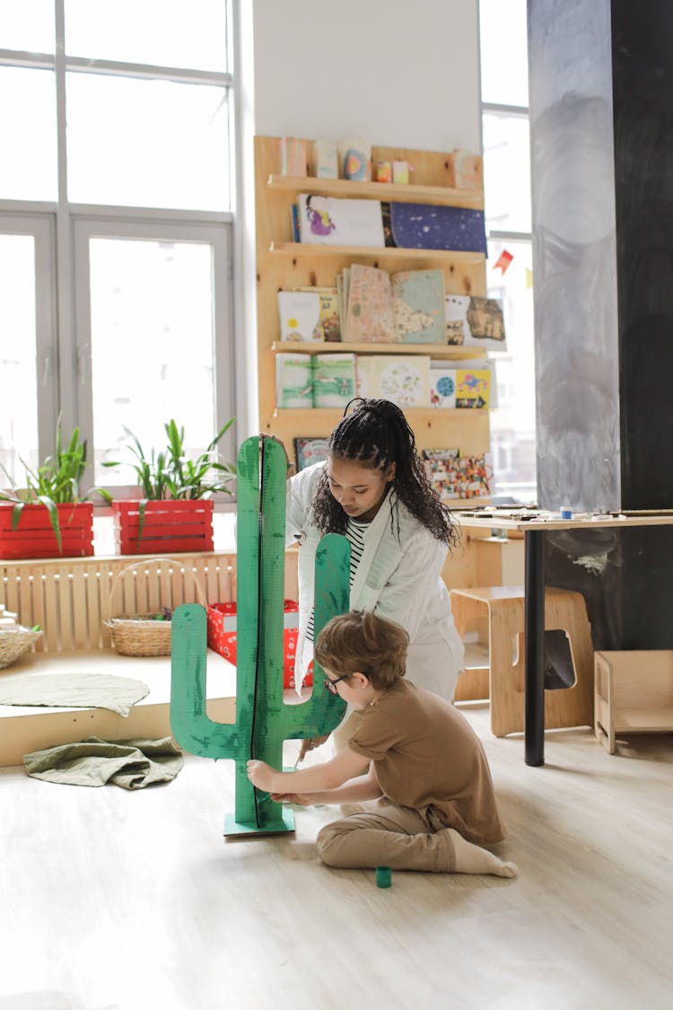 A Teacher Helping Her Student While Painting A Green Cactus