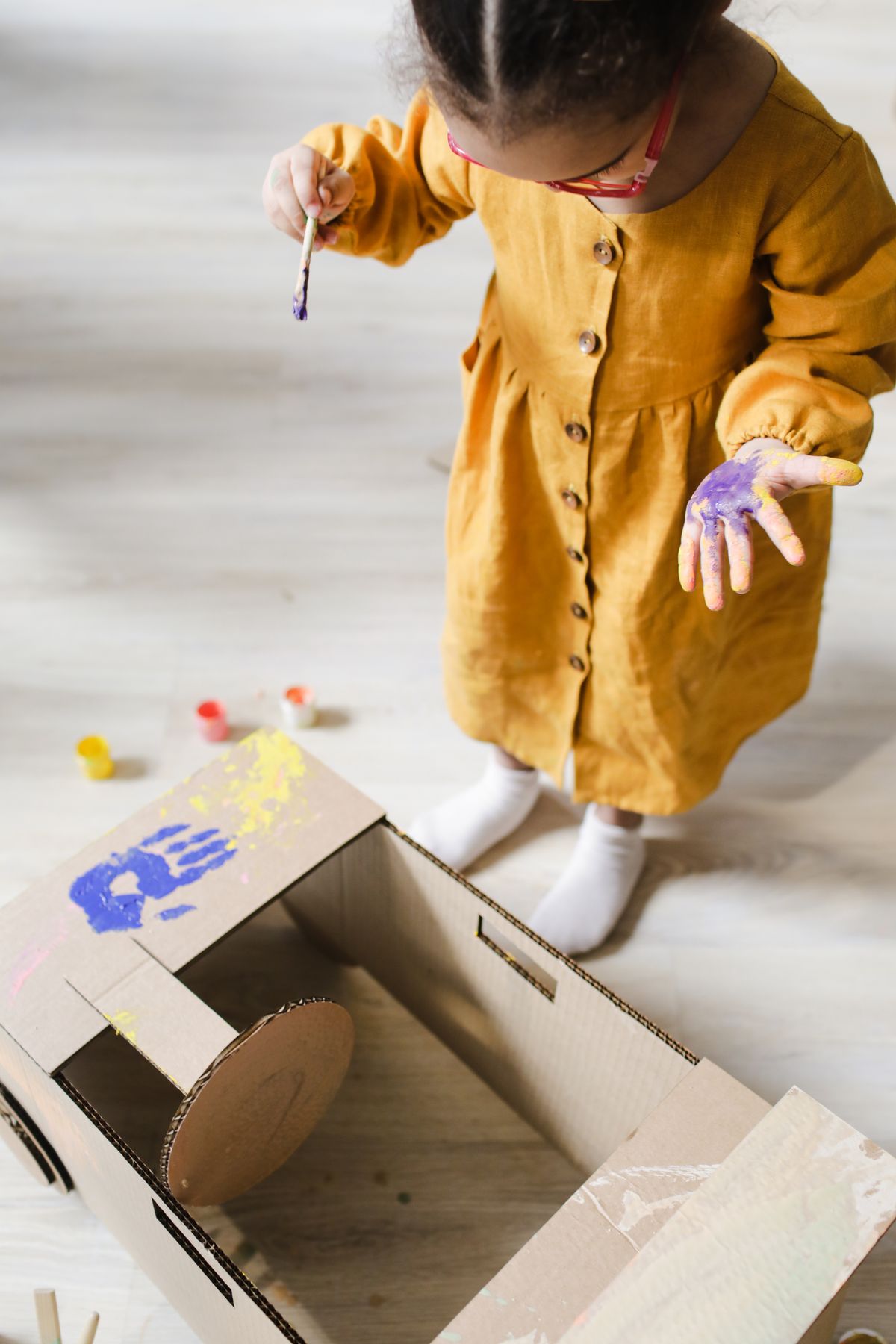 A young girl painting a cardboard box with colorful handprints for horse art
