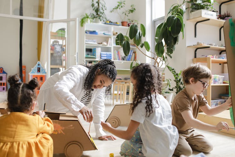 Kids Painting Cardboard Box With Their Teacher