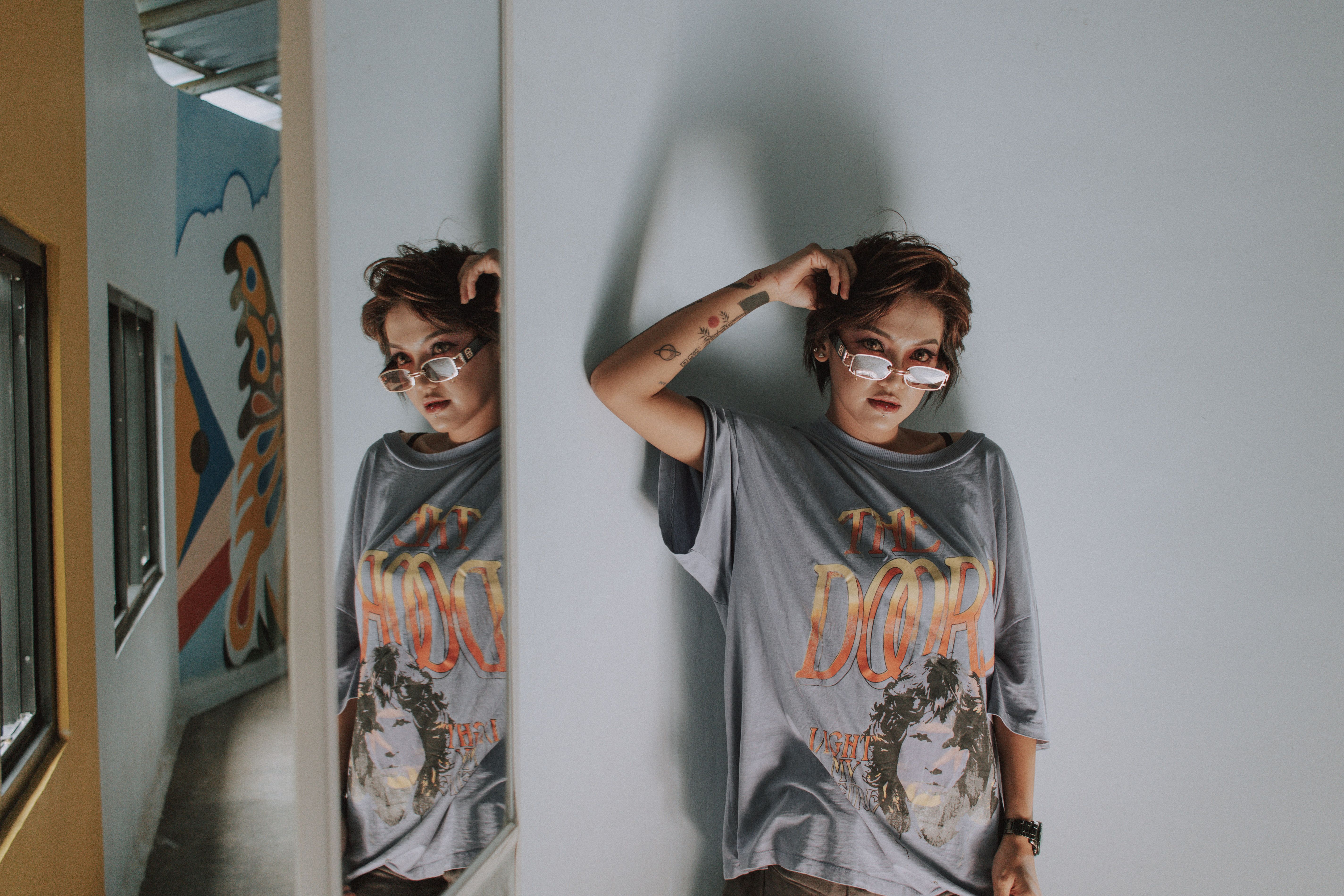 Fashion model in trendy oversized shirt and sunglasses posing indoors with urban art backdrop.