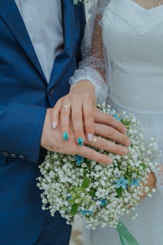 Close-up of a bride and groom holding hands over a delicate wedding bouquet.