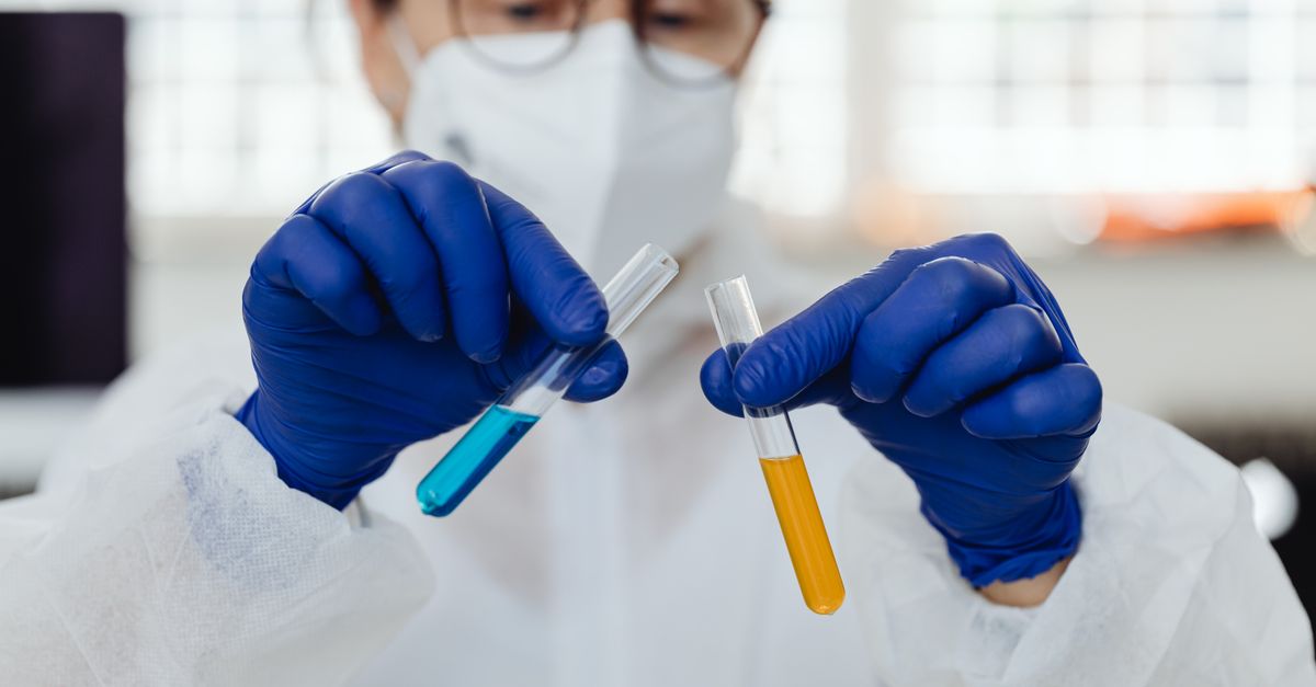 A scientist wearing gloves holds test tubes with colorful liquids in a laboratory setting.