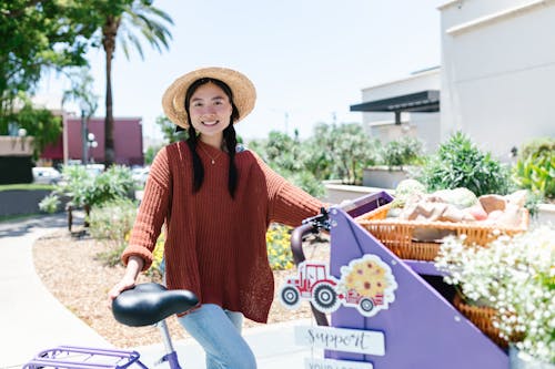 A Woman in Knitted Sweater Smiling while Standing Near the Bicycle Cart