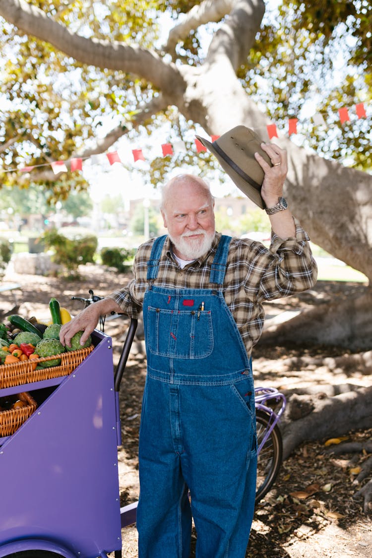 
An Elderly Man Wearing Denim Overalls Holding His Hat