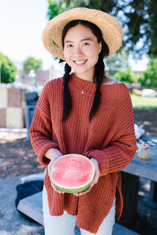 A Woman in Knitted Sweater Smiling while Holding a Sliced Watermelon