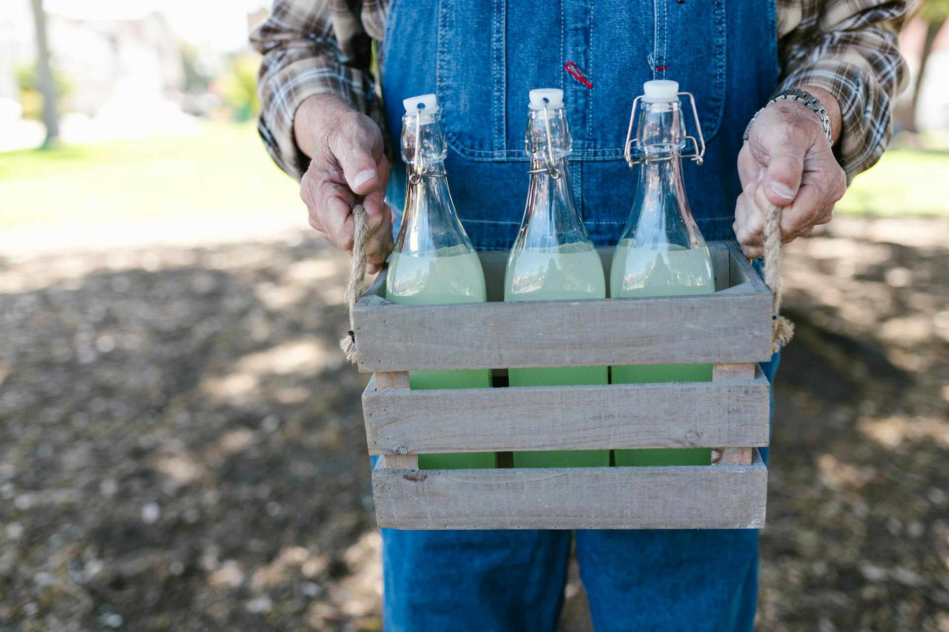 Close-up of farmer holding glass bottles of lemonade in a wooden crate, outdoors.