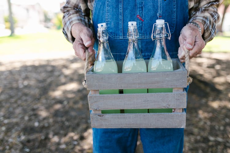 Hands Carrying A Wooden Crate With Glass Bottles 