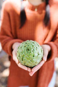 Person holding a fresh artichoke outdoors, showcasing farm-to-table produce.