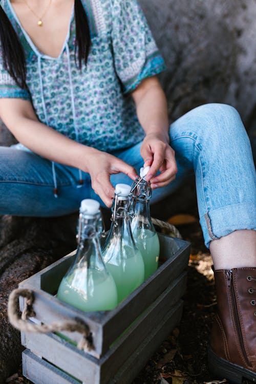 Woman in Blue Denim Jeans Holding Clear Glass Bottle